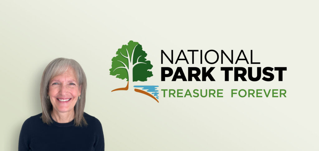 Lisa Stadler smiling in front of the National Park Trust logo